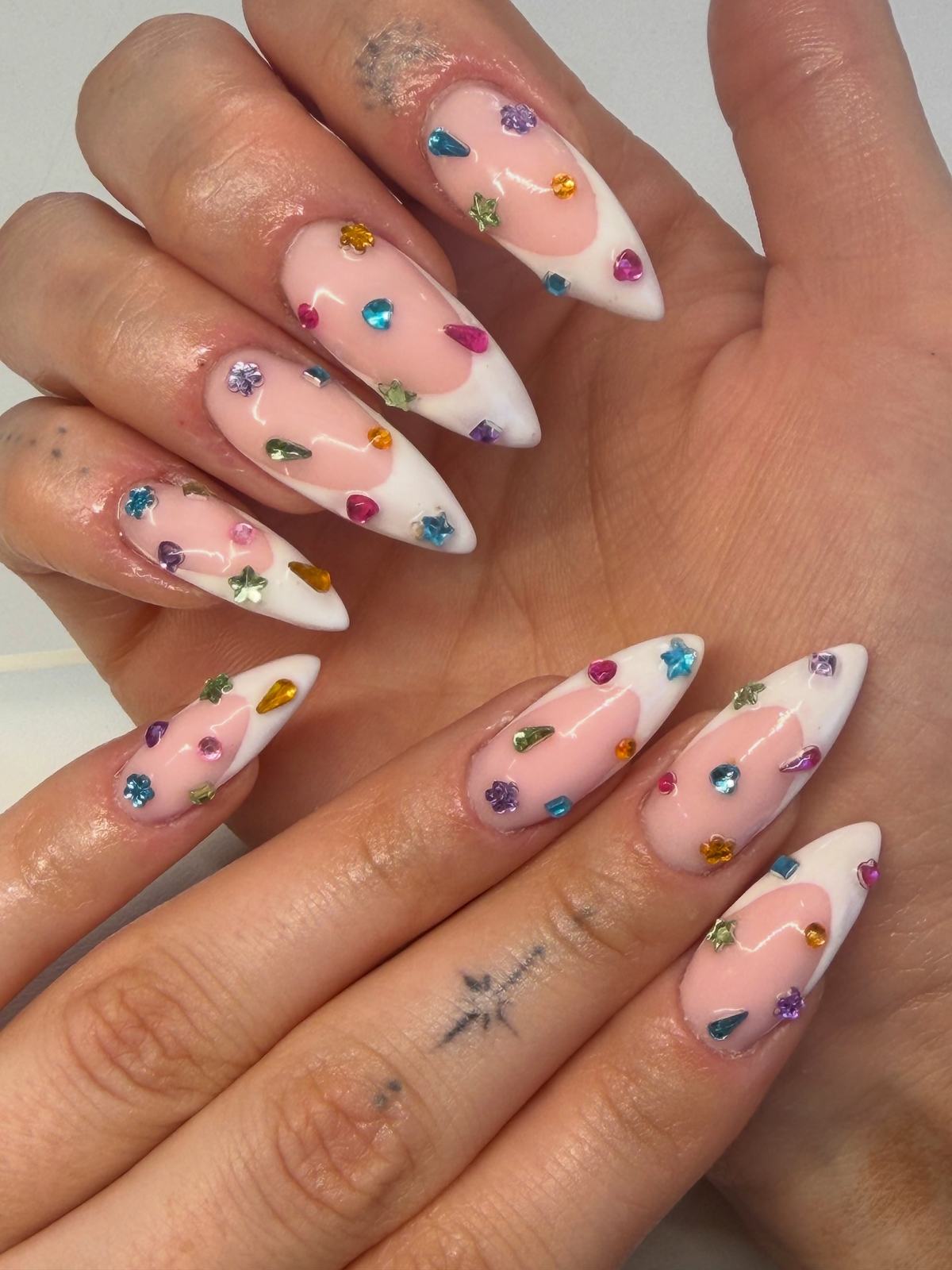 Long stiletto nails with white French tips and scattered coloured gems and rhinestones