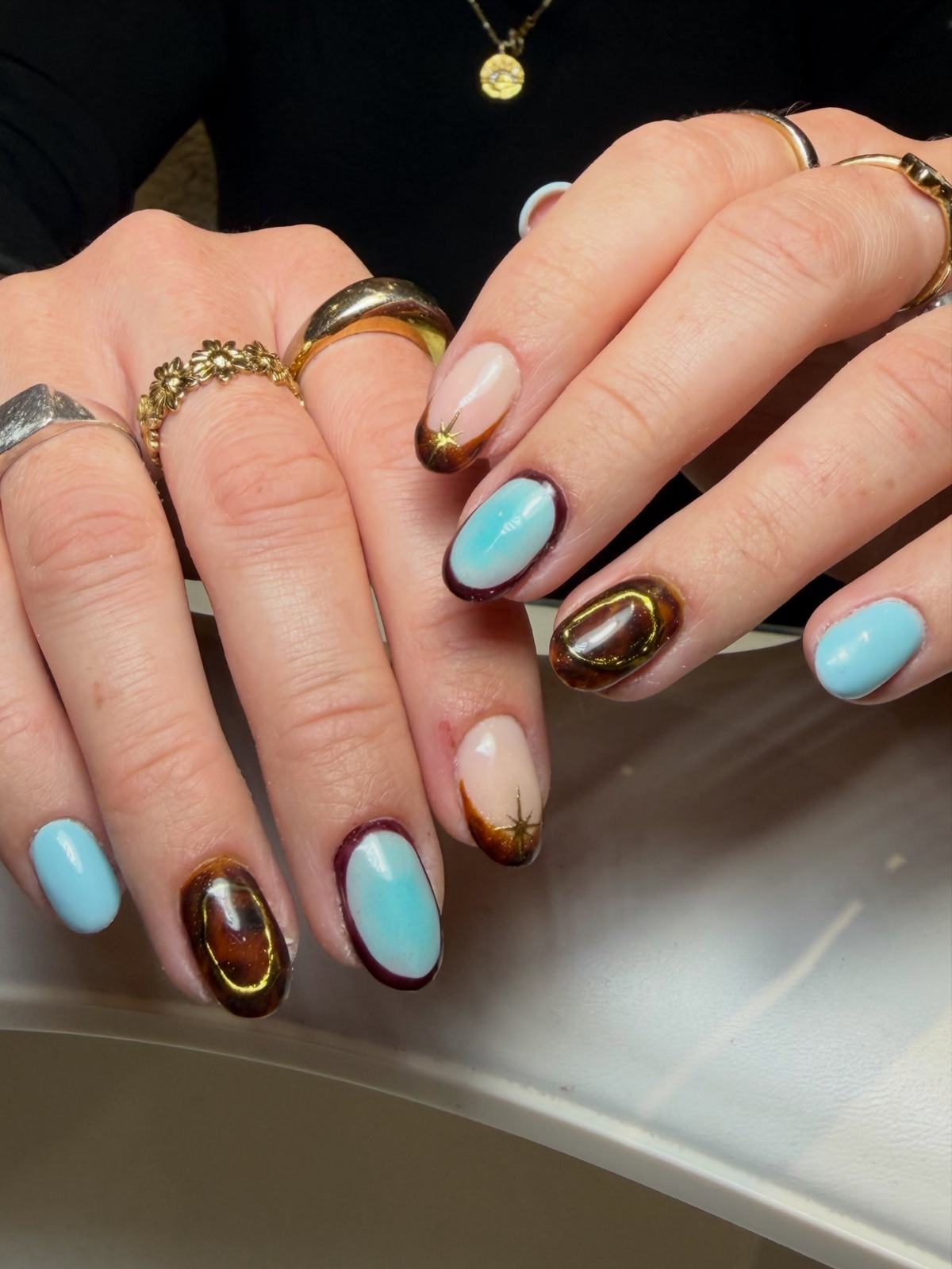 Short almond mix of sky blue with a dark outline, tortoiseshell with gold, and nude with gold star tips